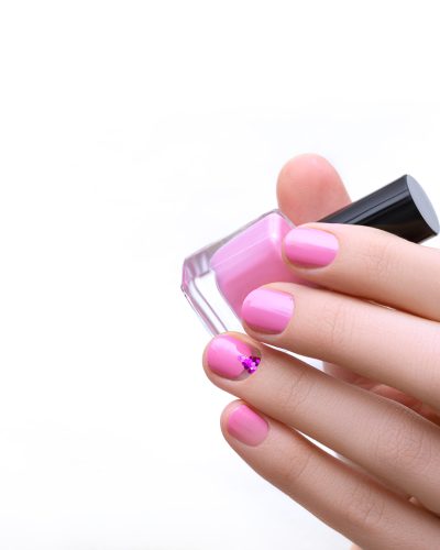 Female hand with pink nail design holding purple nail polish bottle