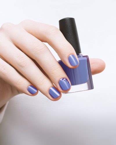 Female hand with purple nail design holding nail polish bottle.